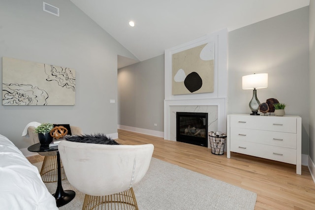 living area with visible vents, baseboards, lofted ceiling, light wood-style flooring, and a tile fireplace