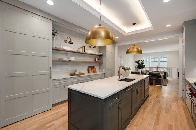 kitchen with light wood finished floors, light stone countertops, open floor plan, an island with sink, and a sink