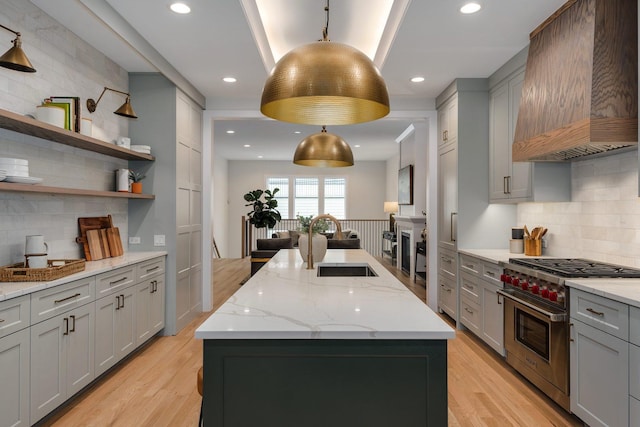 kitchen with designer range, gray cabinets, light wood-style floors, custom exhaust hood, and a sink