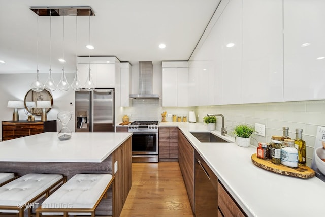 kitchen with a breakfast bar, sink, appliances with stainless steel finishes, white cabinets, and wall chimney exhaust hood