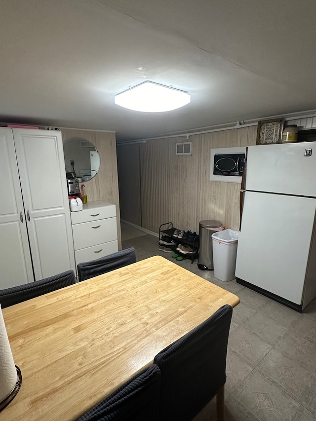 kitchen with white cabinetry, wooden walls, and white fridge