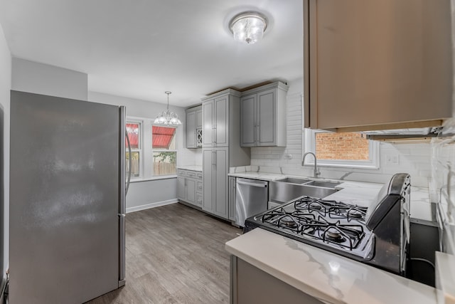 kitchen with backsplash, light hardwood / wood-style flooring, gray cabinets, decorative light fixtures, and stainless steel appliances