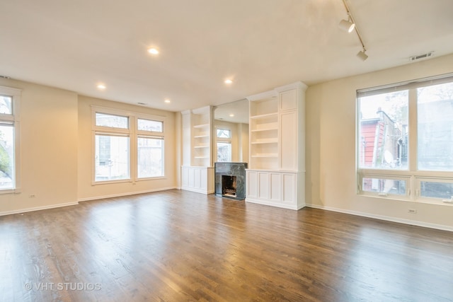 unfurnished living room featuring a wealth of natural light, track lighting, and dark hardwood / wood-style floors