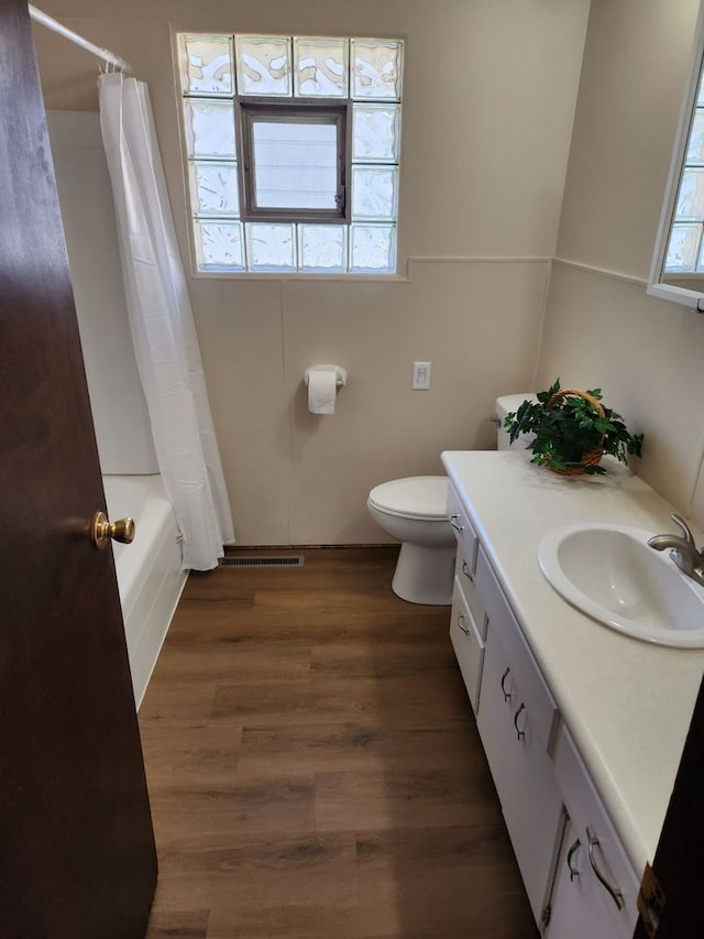 full bathroom featuring hardwood / wood-style floors, shower / tub combo with curtain, vanity, and toilet