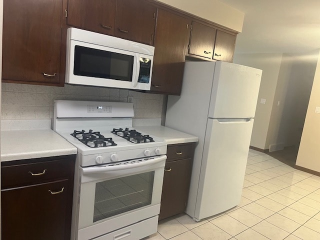 kitchen with dark brown cabinetry, tasteful backsplash, white appliances, and light tile patterned flooring