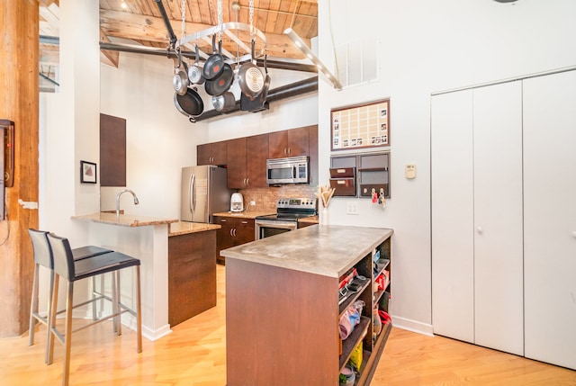 kitchen featuring a towering ceiling, light wood-type flooring, appliances with stainless steel finishes, a breakfast bar, and kitchen peninsula