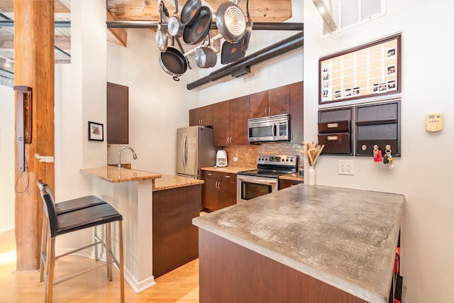 kitchen with kitchen peninsula, appliances with stainless steel finishes, tasteful backsplash, a kitchen bar, and light wood-type flooring