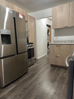 kitchen featuring stacked washing maching and dryer, light brown cabinetry, dark hardwood / wood-style flooring, and stainless steel appliances