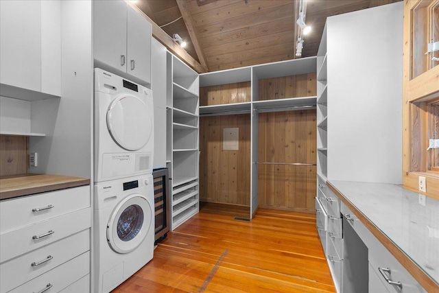 clothes washing area with light wood-type flooring, wooden ceiling, cabinets, and stacked washer and clothes dryer