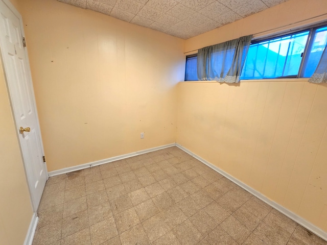 empty room featuring a drop ceiling and wood walls