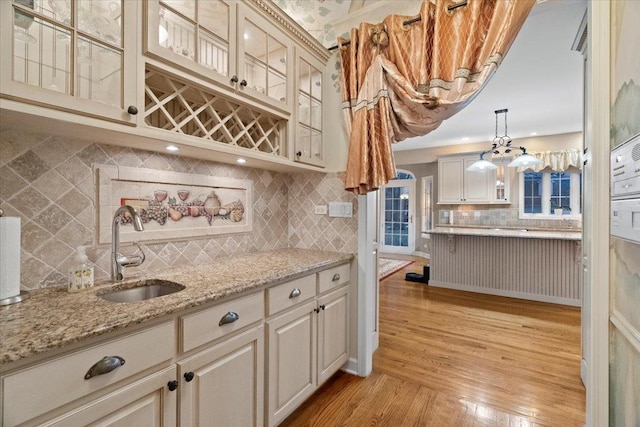 kitchen with sink, tasteful backsplash, light stone counters, decorative light fixtures, and light wood-type flooring