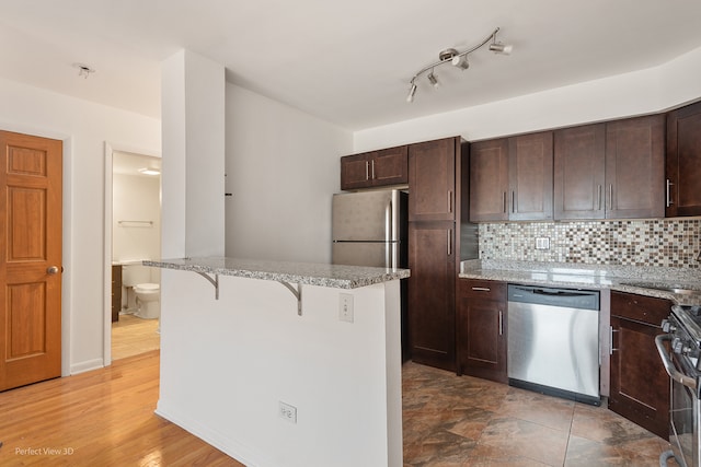 kitchen featuring a breakfast bar, decorative backsplash, appliances with stainless steel finishes, and light hardwood / wood-style flooring