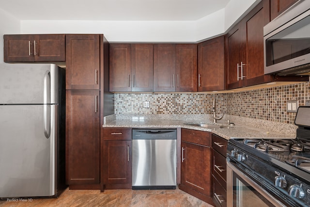 kitchen with backsplash, light stone counters, sink, and appliances with stainless steel finishes