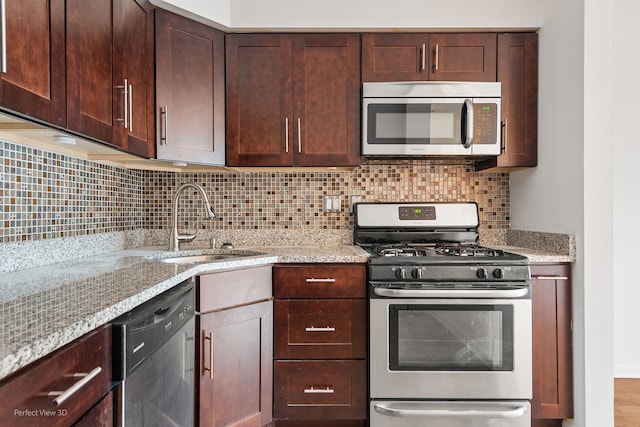 kitchen featuring tasteful backsplash, light stone counters, dark brown cabinets, stainless steel appliances, and sink