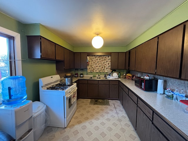 kitchen featuring dark brown cabinets, sink, white gas range oven, and tasteful backsplash