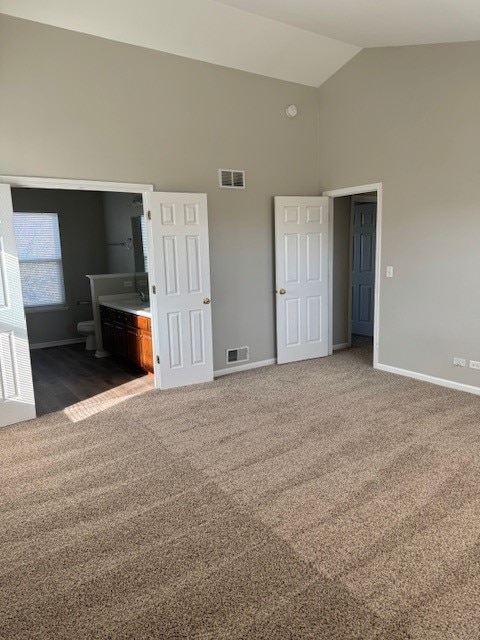 unfurnished bedroom with connected bathroom, high vaulted ceiling, and dark carpet