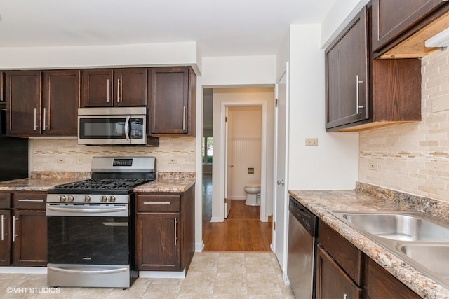 kitchen featuring decorative backsplash, light wood-type flooring, stainless steel appliances, and dark brown cabinetry