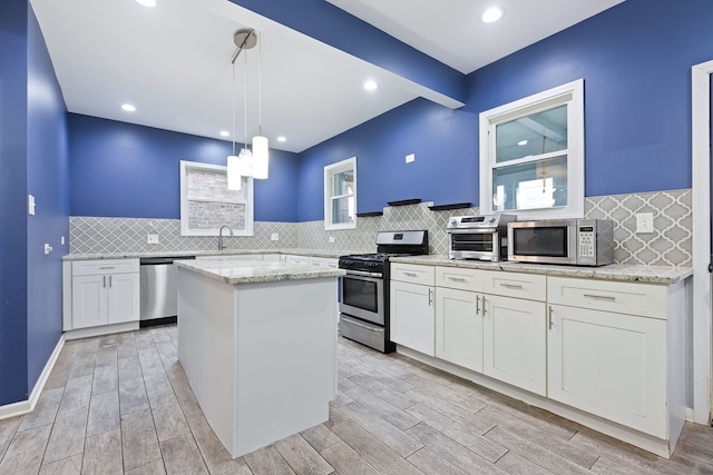 kitchen with a center island, hanging light fixtures, light hardwood / wood-style floors, decorative backsplash, and appliances with stainless steel finishes