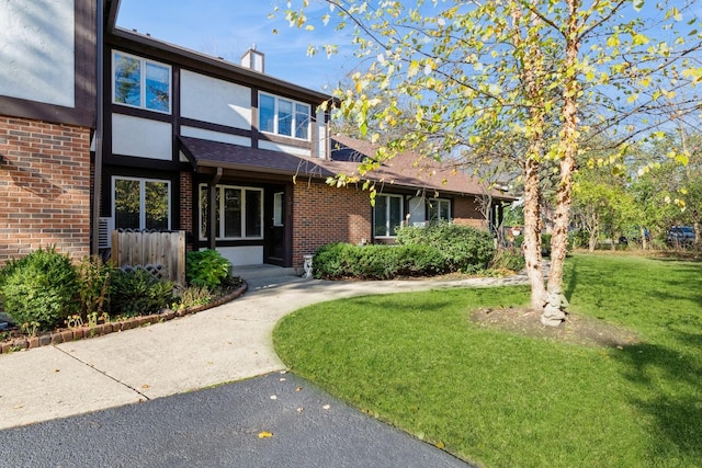 tudor house featuring brick siding, a front lawn, a chimney, and stucco siding