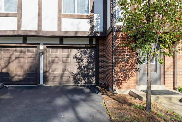 entrance to property featuring a garage, driveway, and brick siding