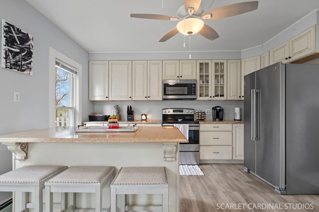 kitchen with appliances with stainless steel finishes, light hardwood / wood-style flooring, a breakfast bar area, and cream cabinets