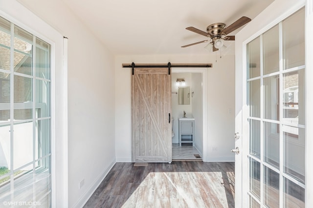 interior space with dark hardwood / wood-style flooring, a barn door, and ceiling fan