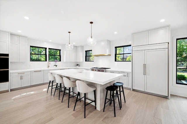 kitchen featuring pendant lighting, a breakfast bar area, paneled built in refrigerator, white cabinetry, and custom range hood