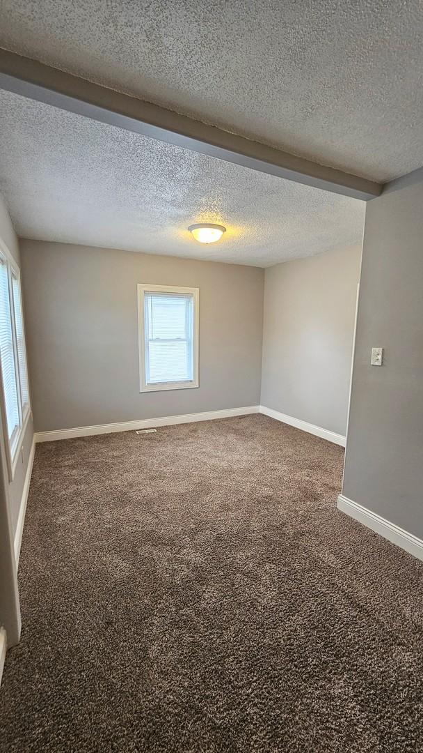 spare room with a textured ceiling and dark colored carpet