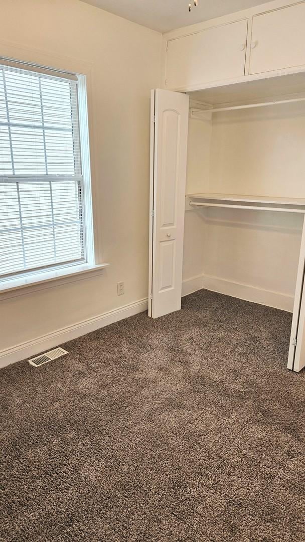 unfurnished bedroom featuring dark colored carpet and multiple windows