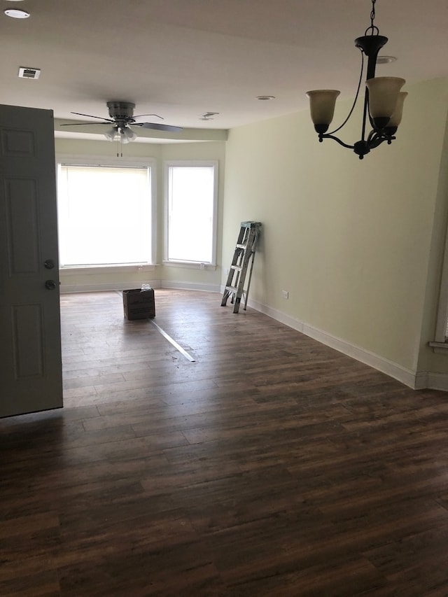 empty room with ceiling fan with notable chandelier and dark wood-type flooring