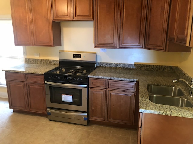 kitchen featuring gas range, sink, light tile patterned floors, and stone countertops