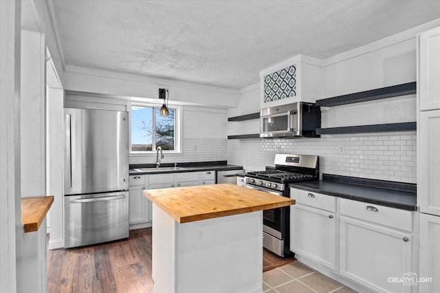 kitchen with a center island, dark hardwood / wood-style floors, appliances with stainless steel finishes, butcher block countertops, and white cabinetry