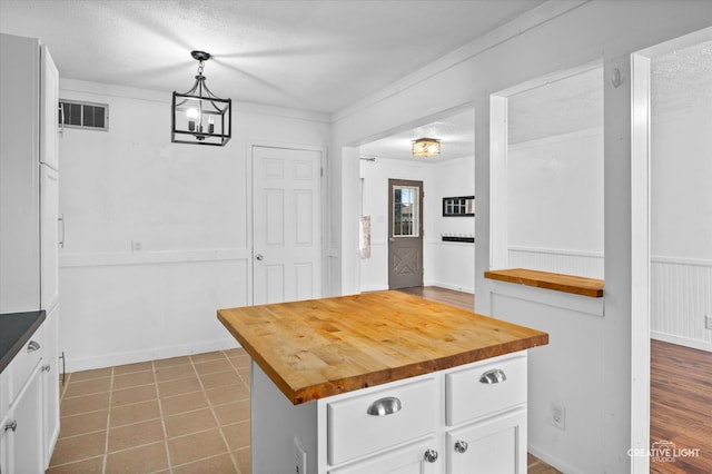 kitchen featuring pendant lighting, wood counters, white cabinets, and a textured ceiling