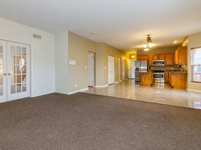 unfurnished living room with an inviting chandelier, light tile patterned floors, sink, and french doors