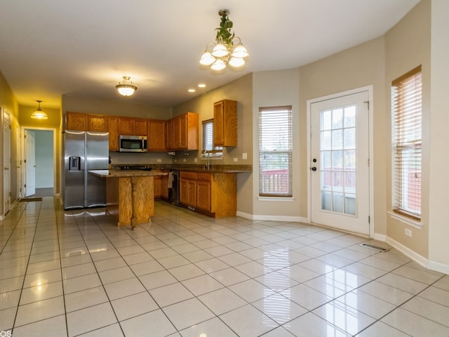 kitchen with appliances with stainless steel finishes, a center island, a wealth of natural light, and light tile patterned flooring