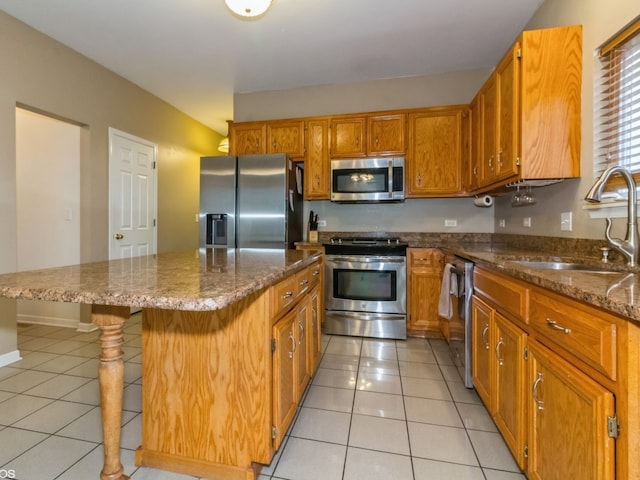 kitchen featuring a kitchen bar, stainless steel appliances, sink, light tile patterned floors, and a center island