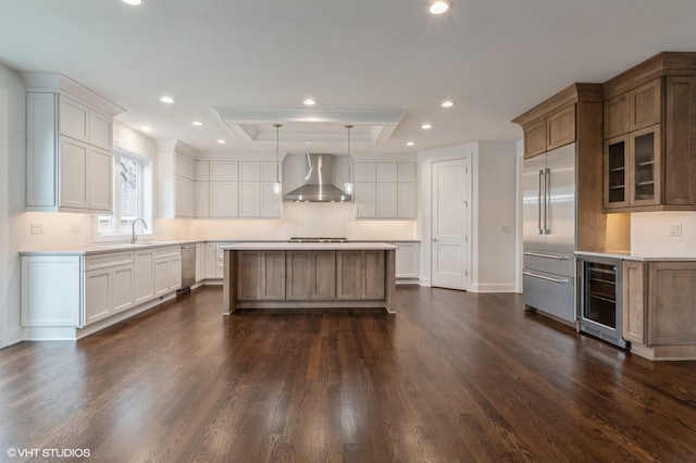 kitchen with beverage cooler, white cabinetry, a kitchen island, hanging light fixtures, and wall chimney exhaust hood