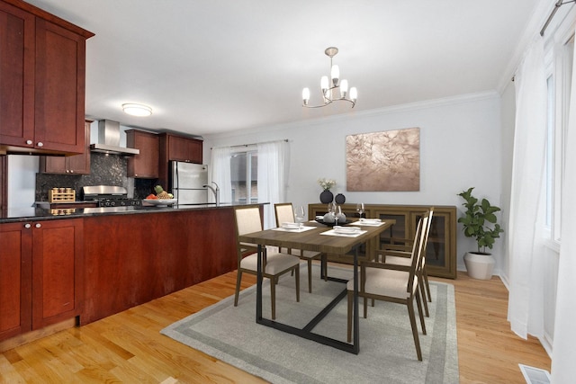 kitchen featuring light hardwood / wood-style floors, wall chimney exhaust hood, a chandelier, and appliances with stainless steel finishes