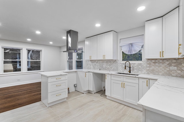 kitchen with island exhaust hood, light stone countertops, backsplash, sink, and white cabinets