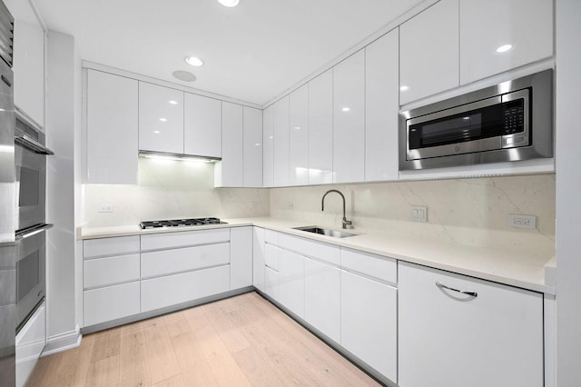 kitchen with sink, appliances with stainless steel finishes, white cabinetry, backsplash, and light wood-type flooring