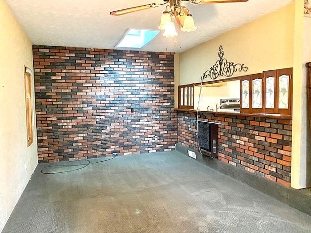 unfurnished living room featuring carpet, a skylight, ceiling fan, and brick wall