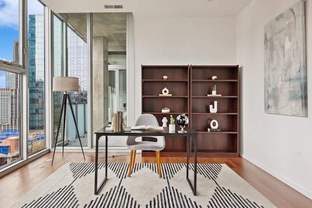 office featuring a healthy amount of sunlight, floor to ceiling windows, visible vents, and wood finished floors