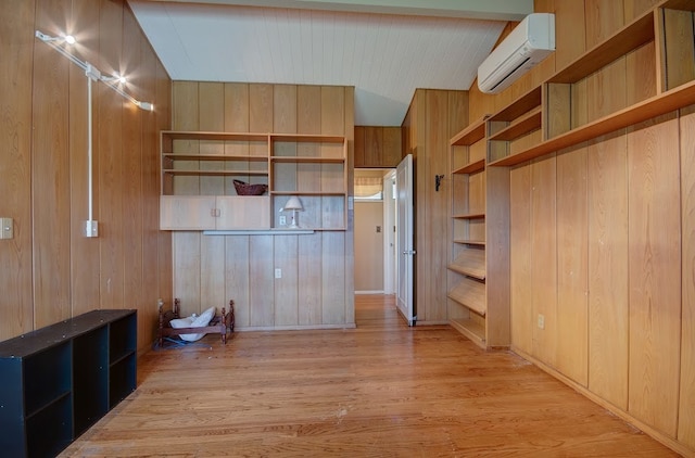 unfurnished living room featuring wood walls, lofted ceiling, light hardwood / wood-style floors, and an AC wall unit