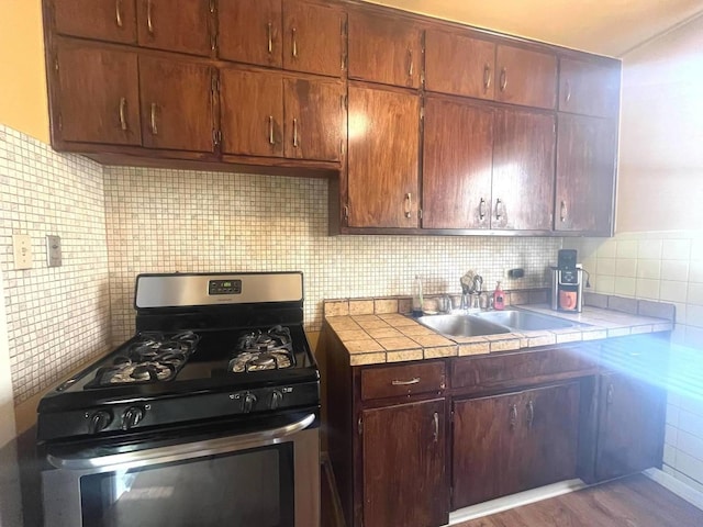 kitchen featuring backsplash, gas stove, sink, tile countertops, and light hardwood / wood-style flooring