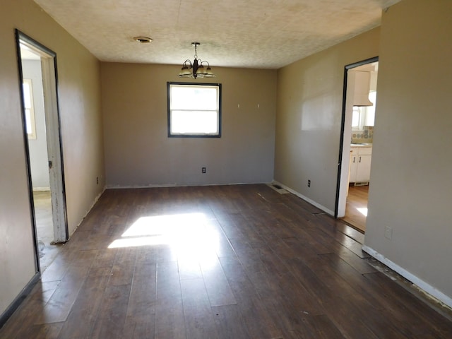 unfurnished room featuring dark wood-type flooring, a textured ceiling, and a notable chandelier