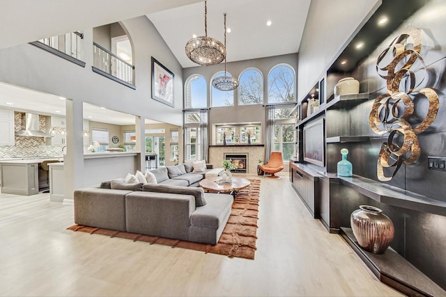 living room with high vaulted ceiling, an inviting chandelier, a wealth of natural light, and light hardwood / wood-style flooring