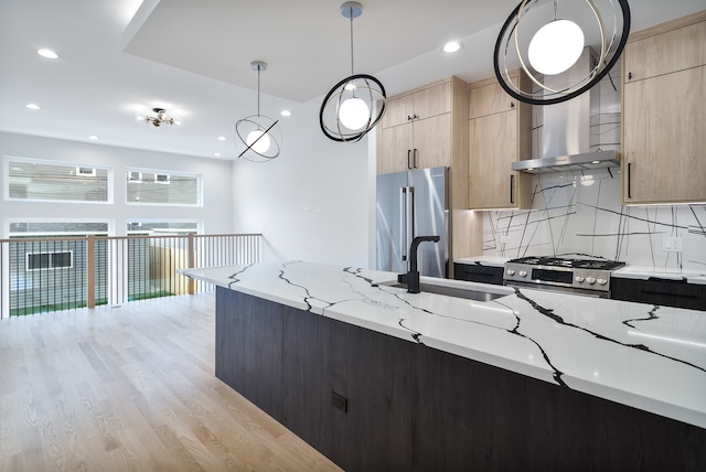 kitchen with light brown cabinets, hanging light fixtures, light hardwood / wood-style flooring, light stone countertops, and stainless steel appliances