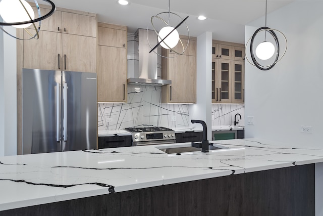 kitchen with pendant lighting, light stone countertops, wall chimney range hood, and stainless steel appliances