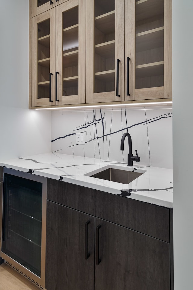 kitchen featuring wine cooler, light stone counters, and sink