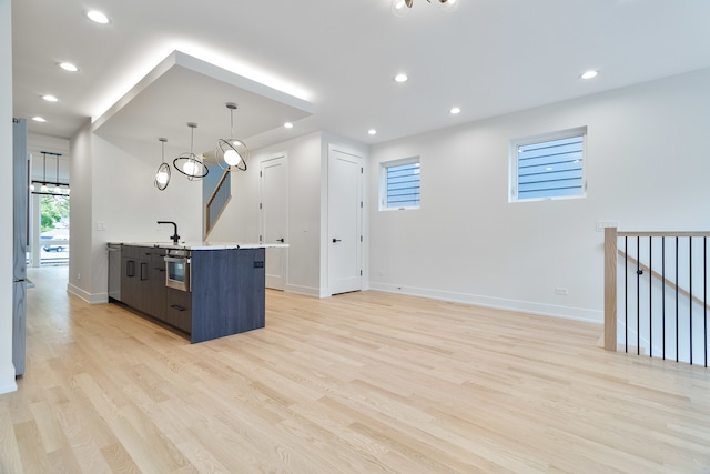 kitchen with light wood-type flooring, sink, pendant lighting, a center island with sink, and oven